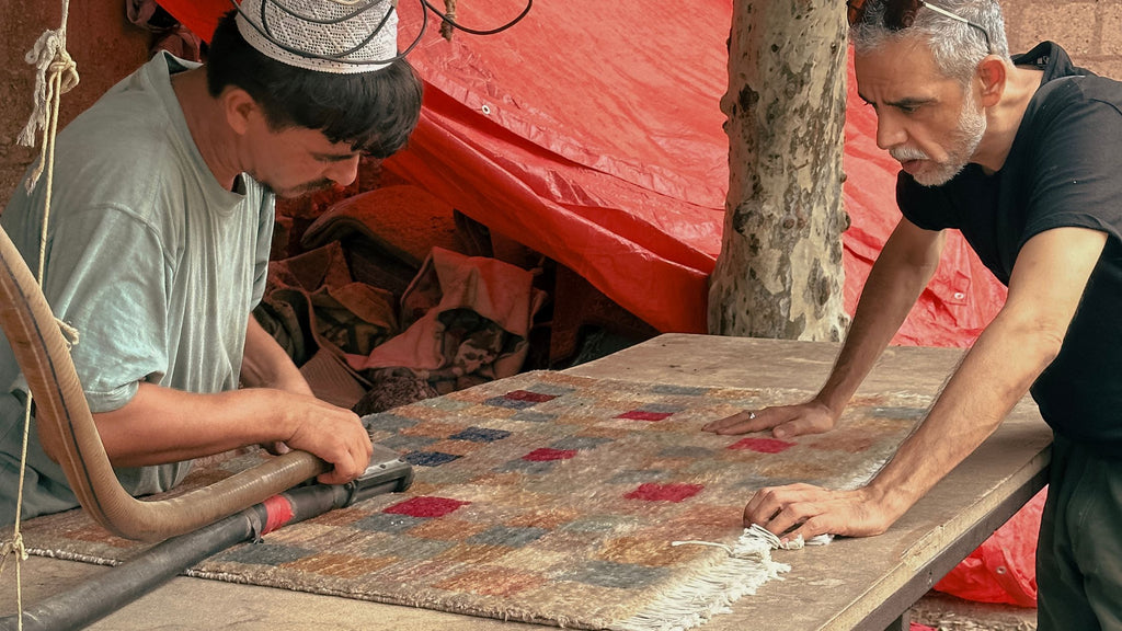 Ahsan Imam with a worker in the factory guiding him how to cut a rug's pile with a machine