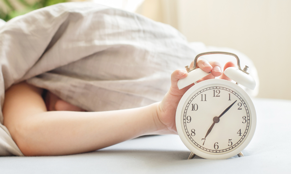 Alcohol sleep disturbance Image of someone pressing the alarm clock from under the Duvet