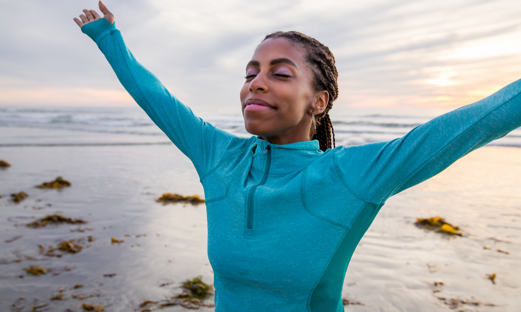 A woman putting her hands up on the beach and taking in the moment of the beauty around her