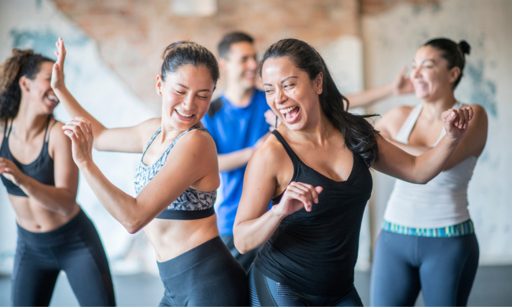 Image of two ladies, doing a dance class, having fun bumping bottoms together