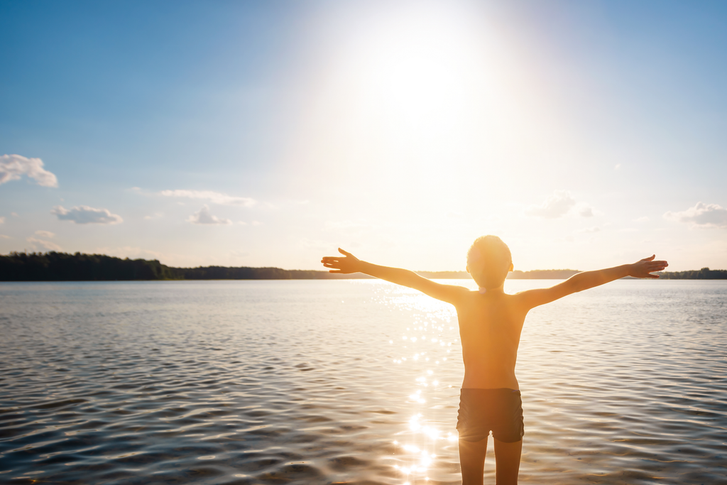 Boy standing my a lake with his arms up to the sun - making Vitamin D
