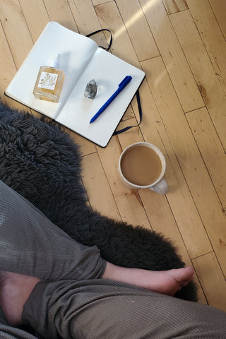 Morning meditation with crystals, coffee, and journal. Woman in soft clothes sitting on sheepskin