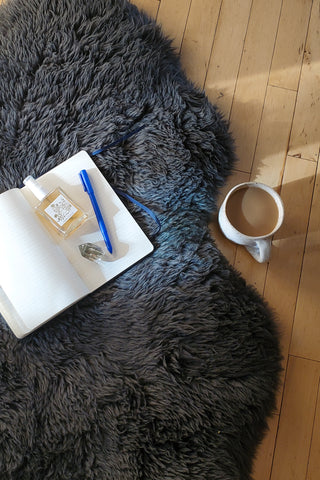 Meditation mist, journal and crystal on sheepskin rug with cup of coffee nearby