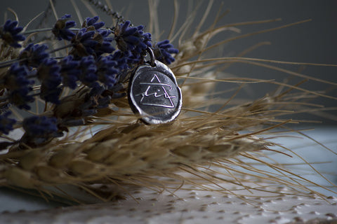 silver medallion layering necklace with air alchemical symbol with wheat and lavender background