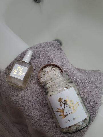 botanical bath salts with linen spray on grey towel at the edge of a bath tub