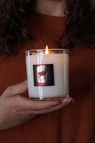 woman in red top with hand holding lit aries zodiac crystal infused soy intention candle