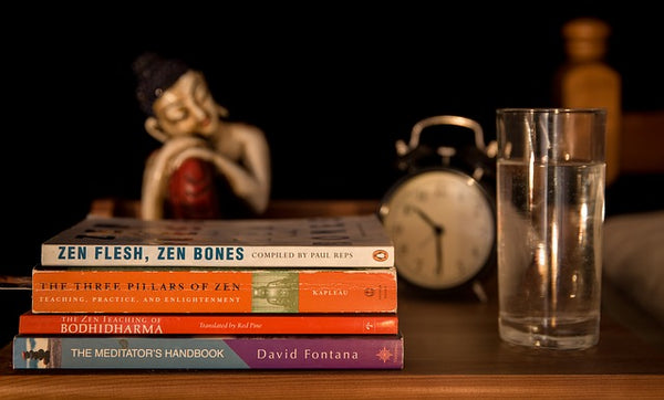 nightstand with books, buddha, and water glass