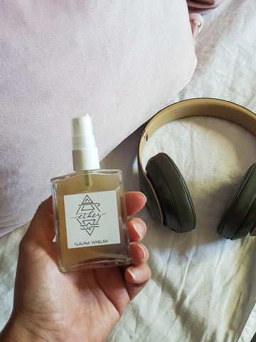 hand holding luxury crystal infused linen spray with white sheets and headphones in the background