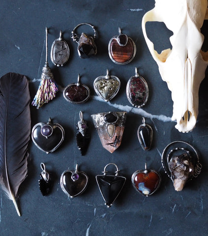 dark healing crystal talisman necklaces with animal skull and feather on black background