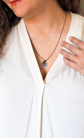 silver fire sign element medallion necklace with orange gemstone detail on woman in white top