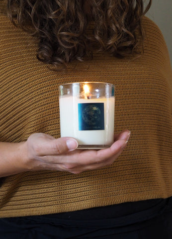 woman in gold knit top holding lit full moon lunar ritual intention candle in palm of hand