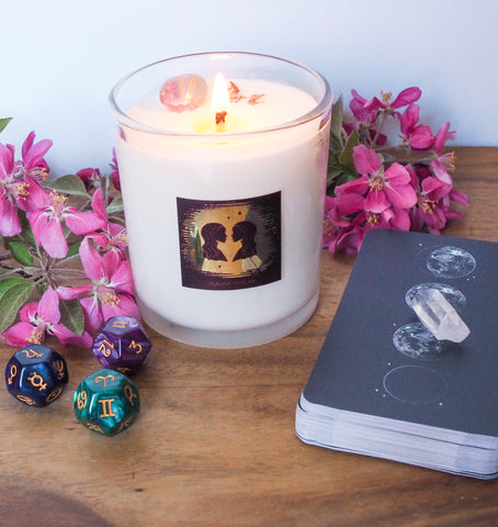 gemini crystal infused soy intention zodiac candle with moon mantra oracle cards, crystals, astrology dice, and pink flowers on wooden tray