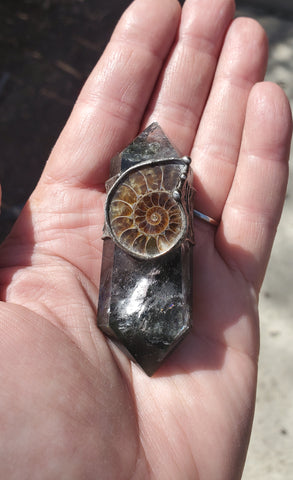 green and clear crystal talisman ritual wand with brown ammonite fossil in palm of hand