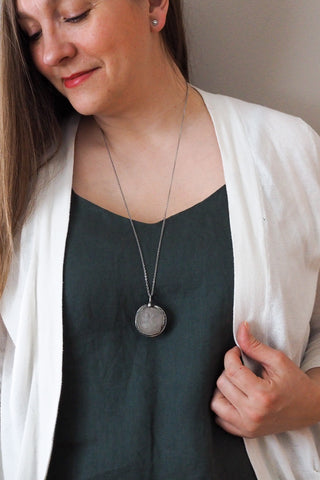 large crystal moon and silver healing crystal talisman necklace on woman in blue top with white cardigan