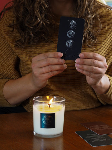 woman in yellow knit top holding lunar oracle cards with lit full moon luxury soy candle burning
