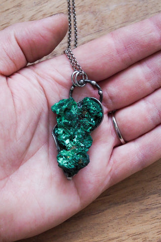 raw green malachite crystal talisman necklace in palm of hand