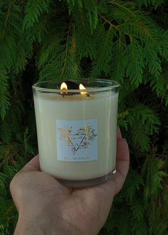 lit petrichor scented earth candle in palm of hand with evergreens in the background