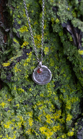 silver boho medallion necklace with red crystal on mossy green and yellow background