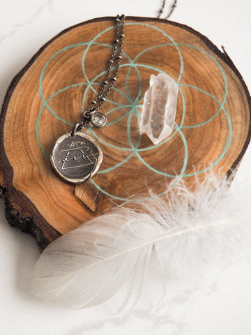 silver air element medallion layering necklace on wood slice with feathers and crystals