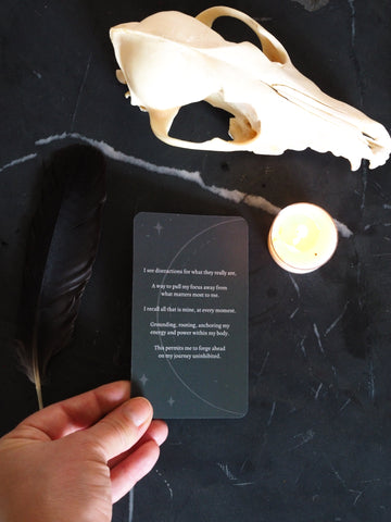 hand holding moon mantra affirmation card on dark background with coyote skull and feather