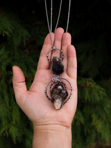 hand holding two dark grey rustic healing crystal talisman necklaces