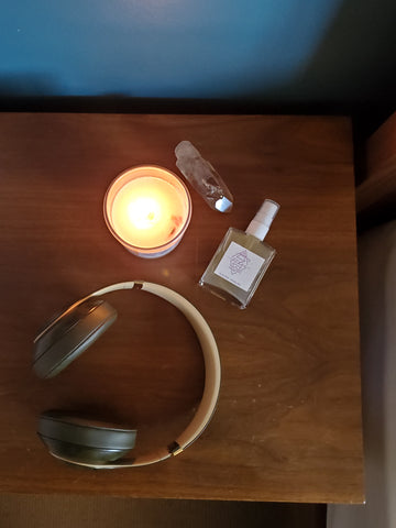 top view of luxury soy crystal candle ritual mist raw gemstone and headphones on wooden nightstand