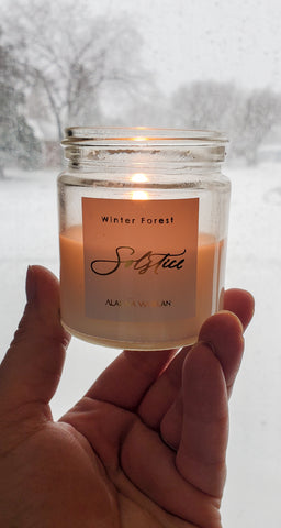hand holding lit luxury soy winter solstice crystal intention candle with snowy background