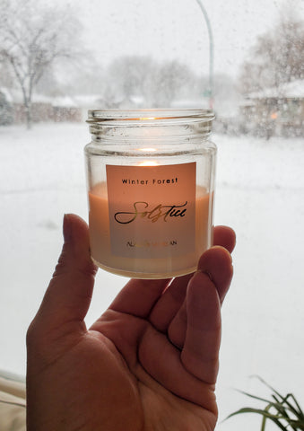 hand holding lit winter solstice luxury soy crystal candle with snowy background