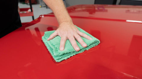 wiping off excess wax from a car with a microfiber towel 