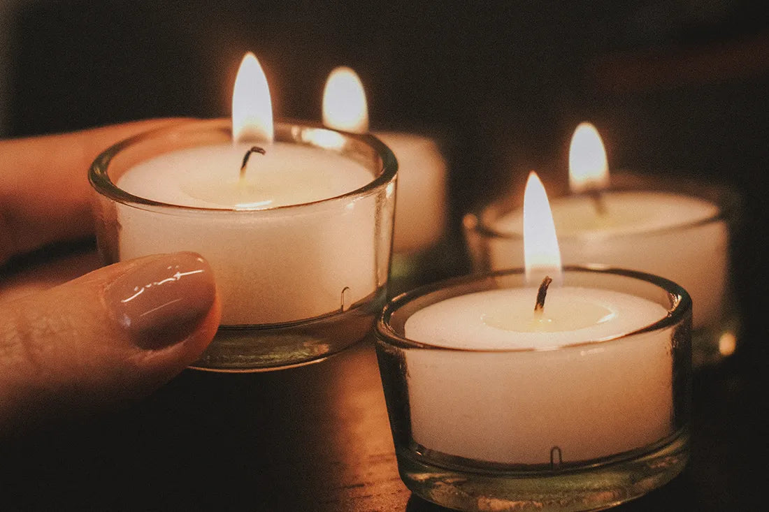 A young woman's hand reaches for a sustainable tealight without a case in a glass tealight holder from WingGuard.