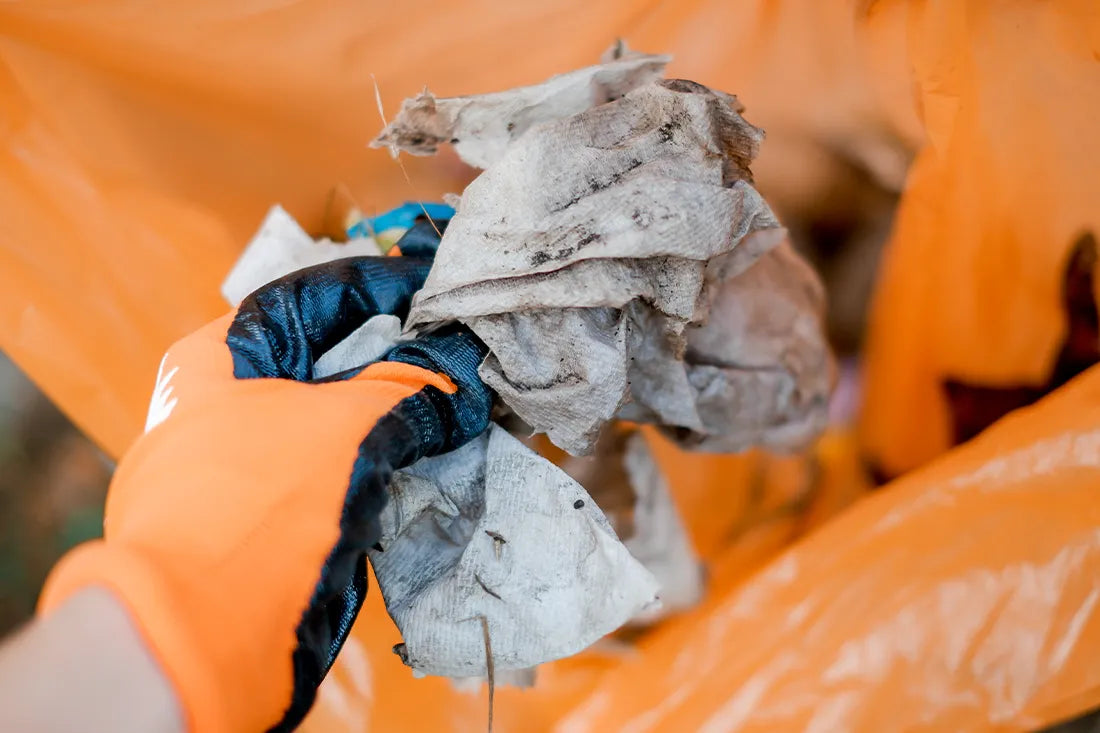 Eine Hand im Kölle-Putzmunter-Handschuh wirft Müll in einen Beutel