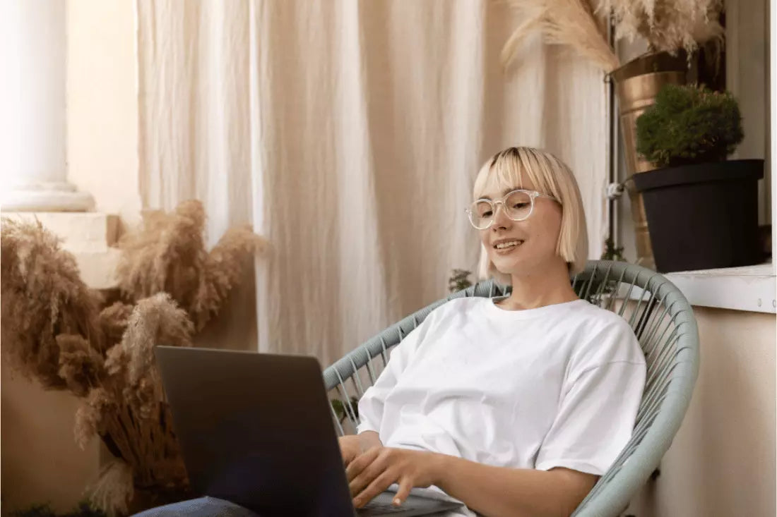 Young woman sits in a wicker chair and works on her laptop from home.