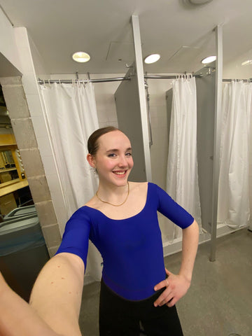 Romy Adair of the Hard Corps Podcast wearing a long sleeve blue leotard in a bathroom for an audition