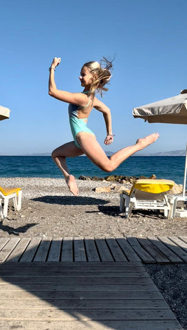 Blonde ballerina wearing blue high neck zip front leotard jumping on the beach