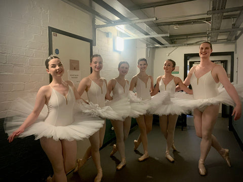 group of women dancers including onme trans women ballet dancer in swan lake costume about to perform on stage