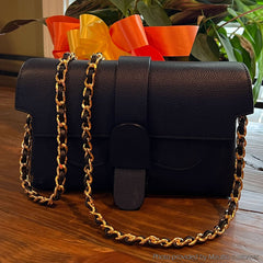 Photo of elegant chain strap with leather woven-in by hand, draped over a black bag.