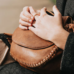 Brown leather saddle bag in the lap of a person.