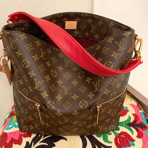 Red leather shoulder strap on customer's LV handbag.