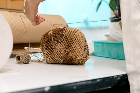 A brown paper parcel is lovingly being wrapped up on a table in Sarah's studio. The twine is being pulled. The parcel is wrapped in sustainable wrapping.