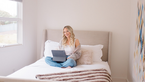 Brandi sitting on a bed while using an iPad.