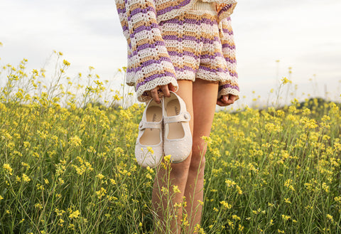 girl holding a pair of swiss dot beige mary janes on the prairie