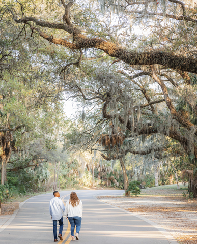 engaged couple walking down a road surrounded by beautiful canopying oak trees