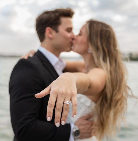 newly engaged couple kissing and flashing their engagement ring to the camera