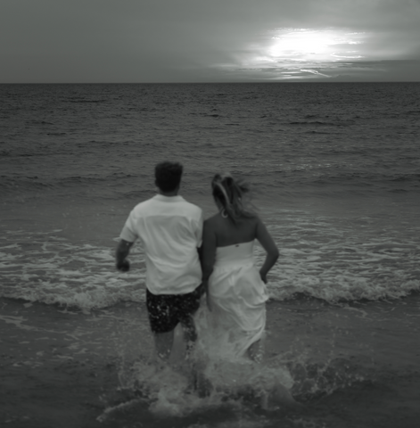 cute couple running into the water at the beach at sunset black and white photo