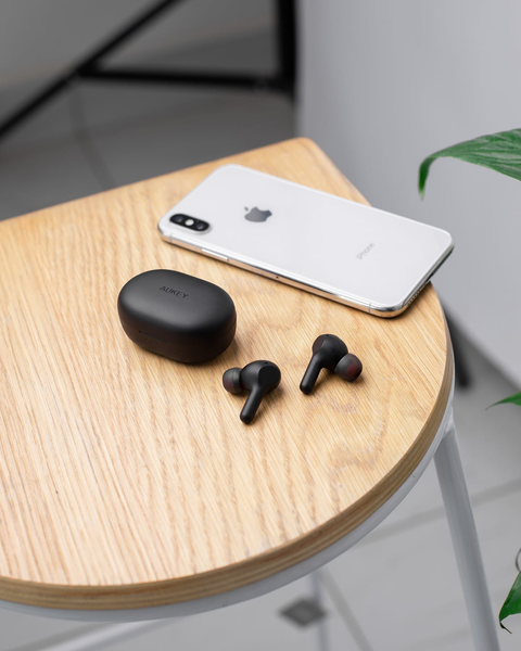 Black Bluetooth earbuds with their case on wood table, with an iPhone.