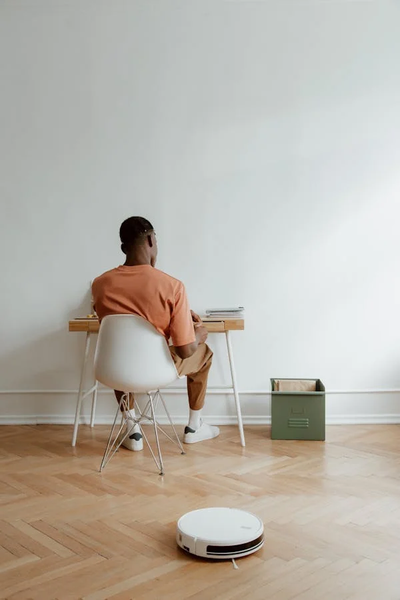 A gentleman is Busy on his books&nbsp; while a Robot vacuum is cleaning the floor