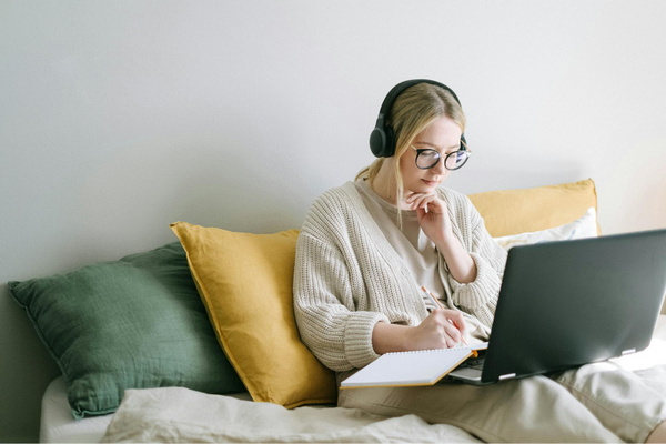 A Lady reading while writing down, using Headphones for noise cancelation