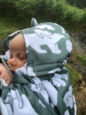 baby fast asleep in a sling. Over the baby is a grey green babywearing cover in a polar bear design. it is raining