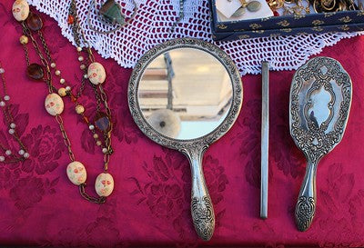 nappe rouge bordeaux sur laquelle sont posés des miroirs à main anciens (un rond et un ovale) ainsi qu'un collier de perles de bois