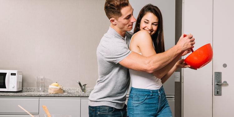 man hugs his girlfriends, the woman's is holding a red bowl